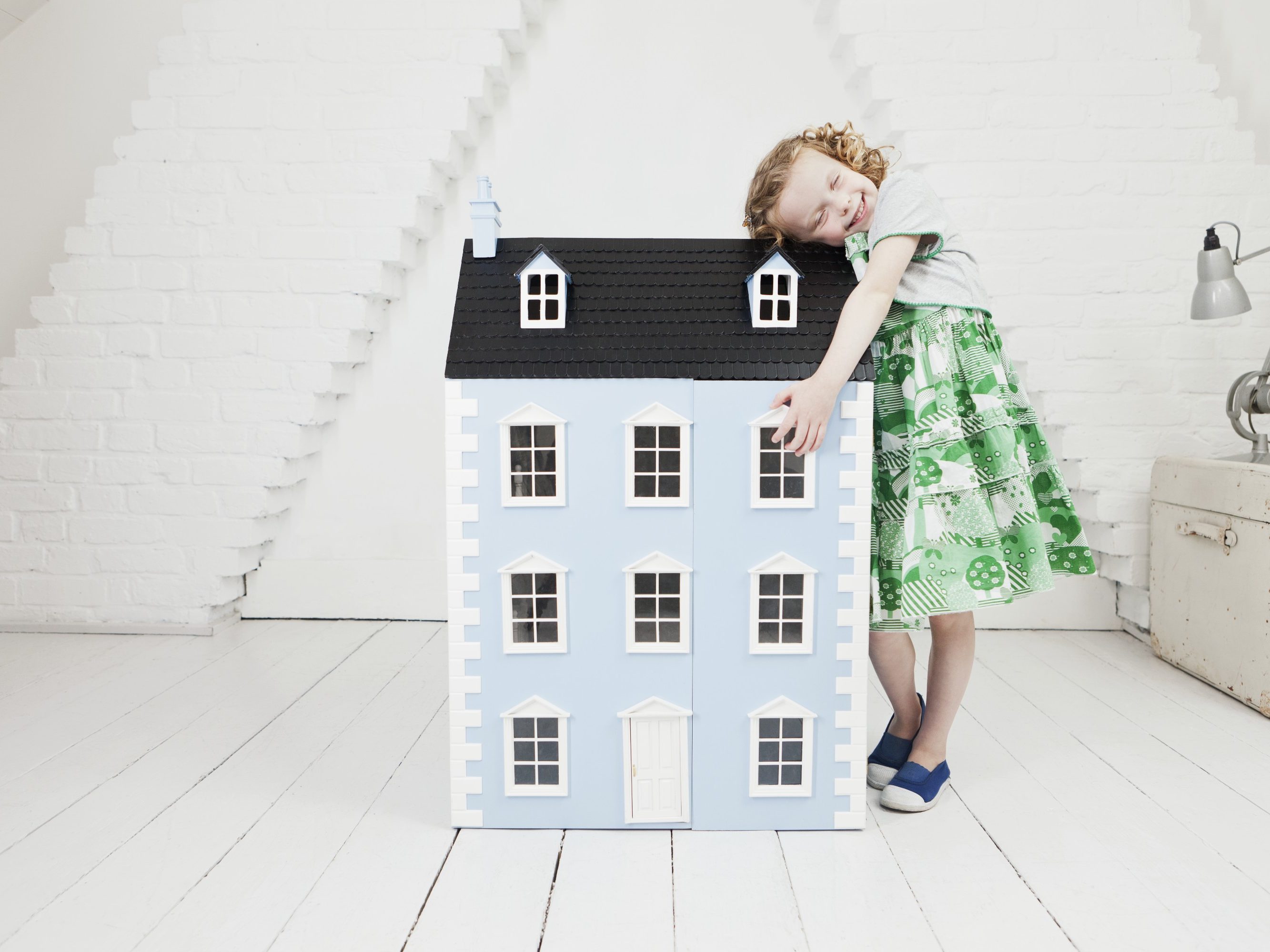 Happy girl leaning against doll house in attic loft