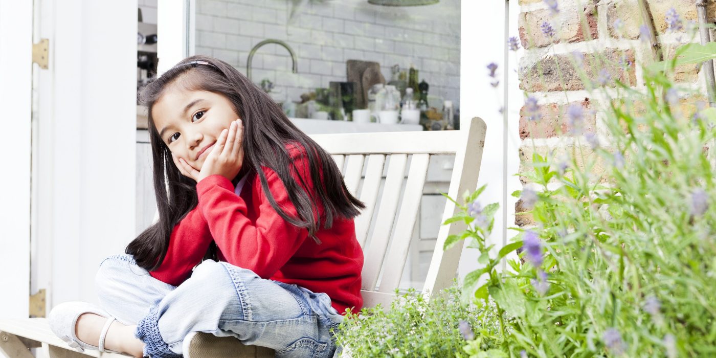 Smiling girl sitting on a wooden bench on patio in front of a brick-lined house