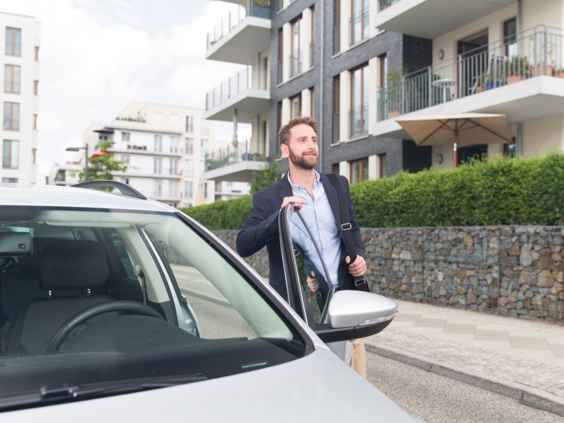 Man with messenger bag at car door in new built housing estate