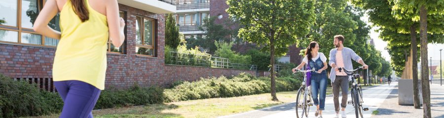 Couple pushing bicycles and woman jogging in a newly built housing estate